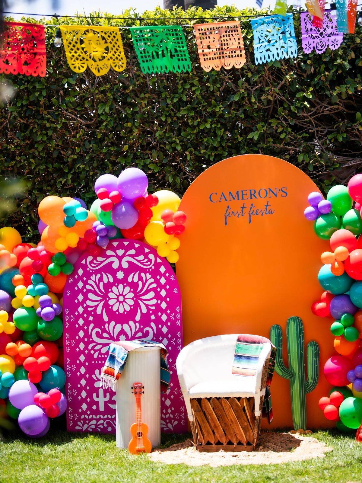 Colorful fiesta backdrop with a rainbow balloon garland and cactus cutouts