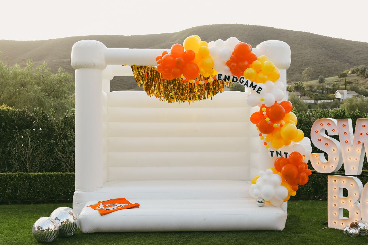 White bounce house with an orange and yellow balloon garland