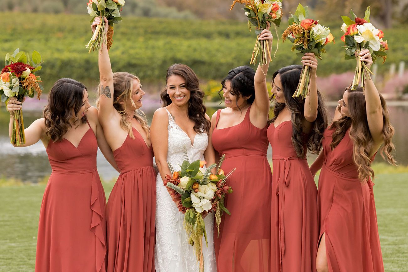 Bridesmaids holding fresh bouquets in rust dresses at a vineyard