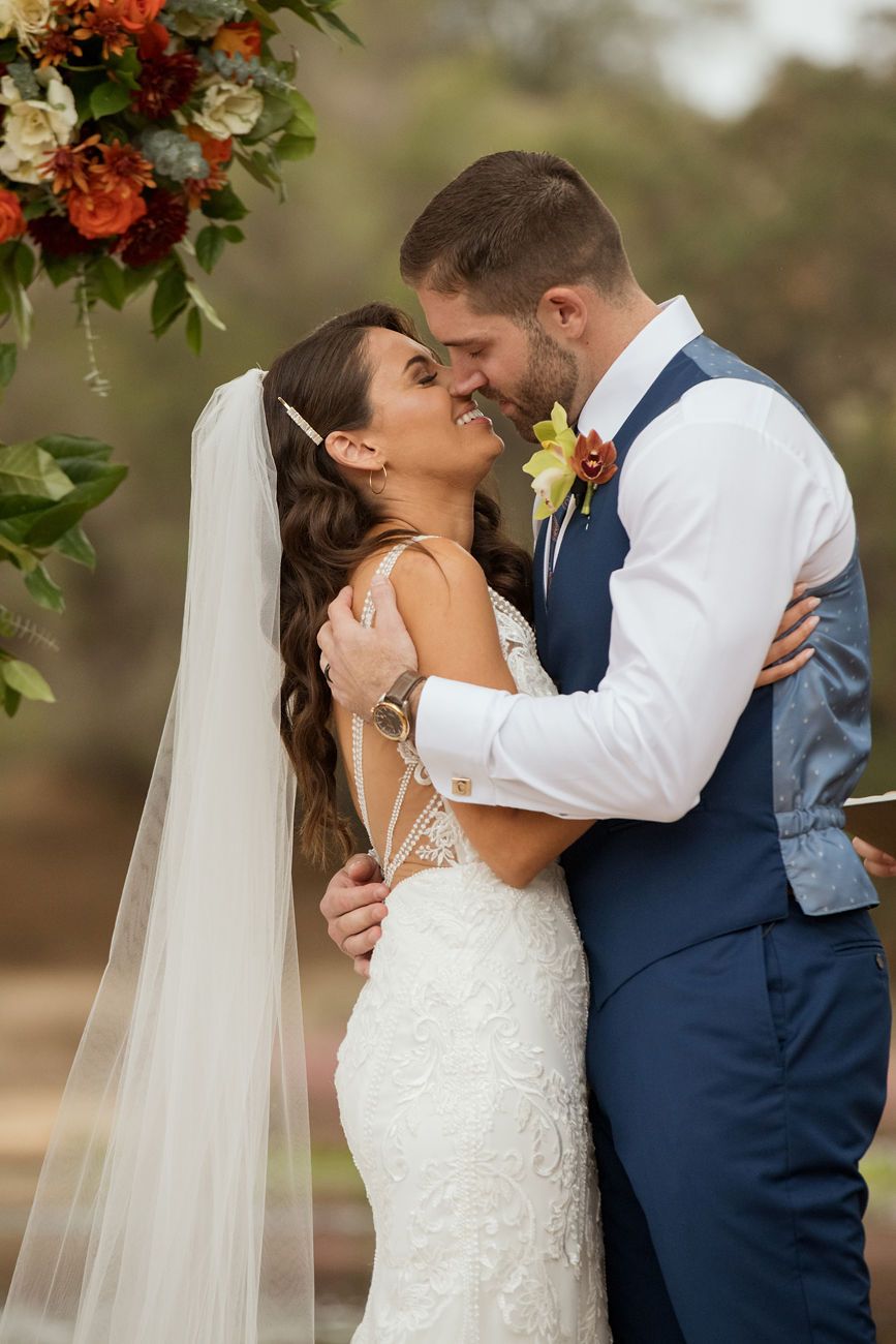 Couple kissing under a wooden ceremony arch with fresh florals