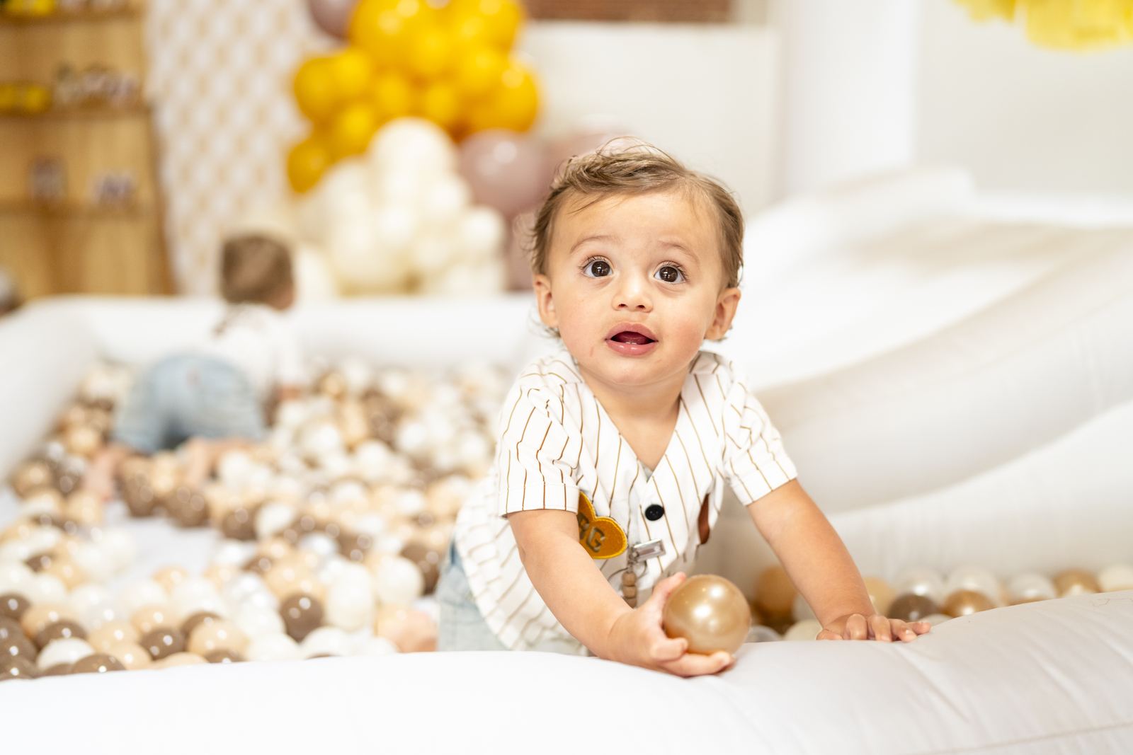Toddler playing in a neutral ball pit at a baseball party